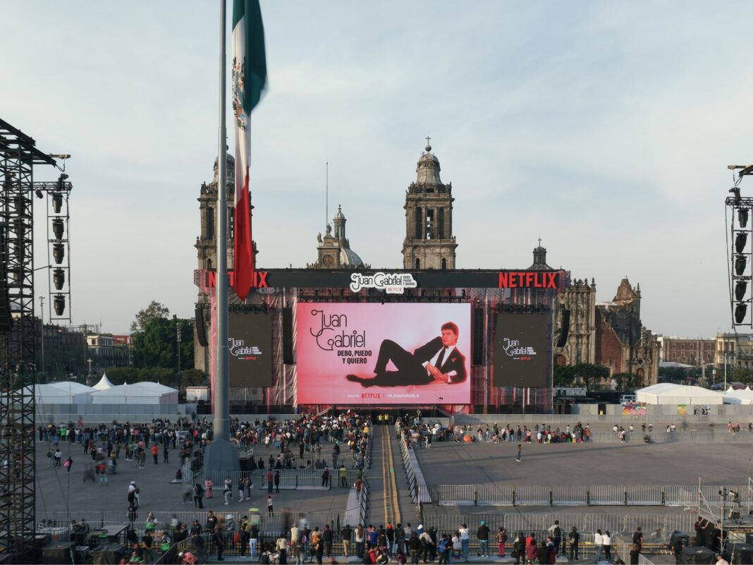 Vista de la plancha del Zócalo de la CDMX llena de gente durante el evento de Juan Gabriel y Netflix, con el escenario y la Catedral Metropolitana al fondo.