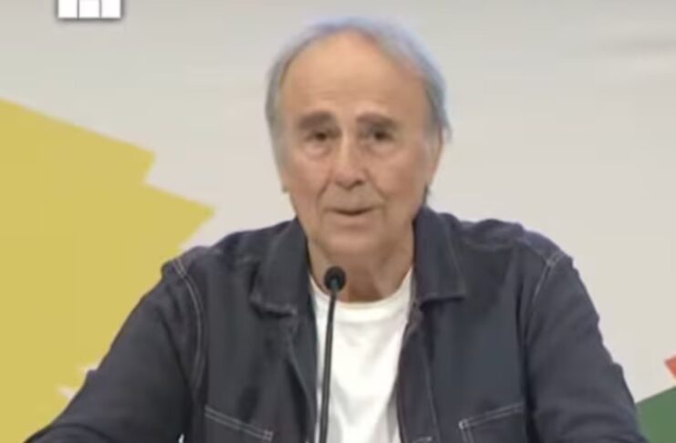 oan Manuel Serrat sentado frente a un micrófono durante su charla en la FIL Guadalajara, vistiendo una chaqueta de mezclilla oscura y camiseta blanca, con expresión seria