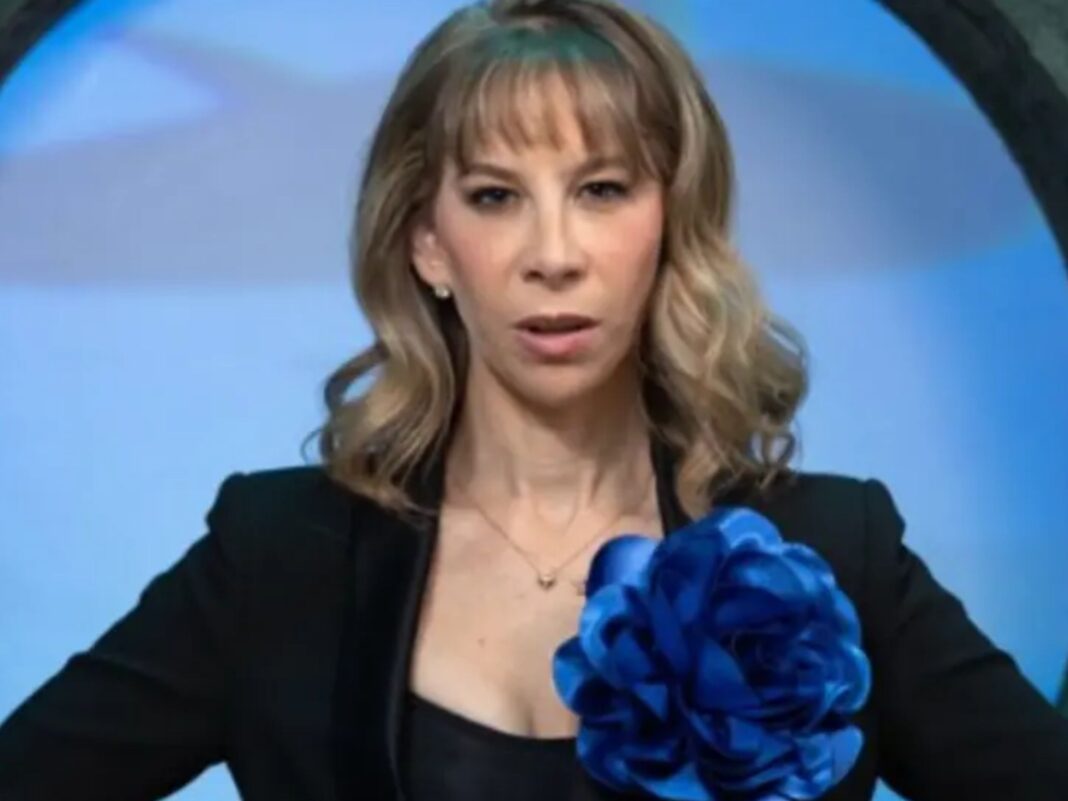 Karla Berman, empresaria e hija de Shanik Berman, mirando a la cámara con expresión seria, vistiendo un saco negro con una flor azul grande en la solapa