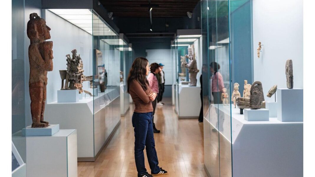 Persona observando una colección de arte prehispánico en las salas del Museo Amparo en Puebla; nota sobre entrada gratuita en invierno.