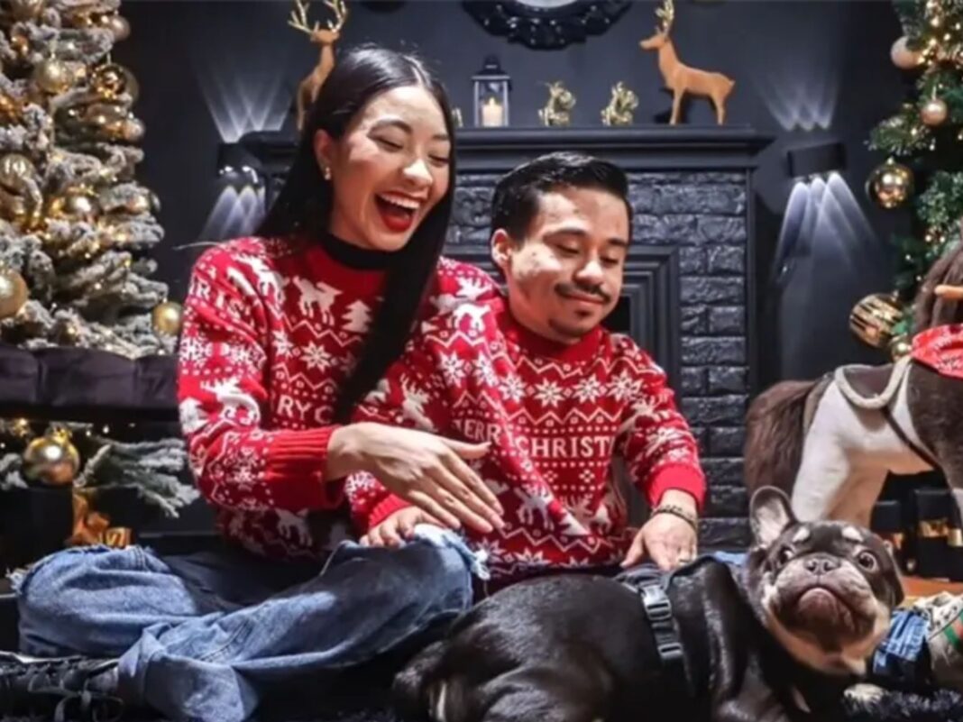 Aranza Salazar, novia de Abelito, sonriendo junto al influencer y su perro frente a un árbol de Navidad usando suéteres rojos.